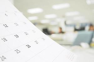 Close up white paper desk calendar on table with blurred office interior background photo