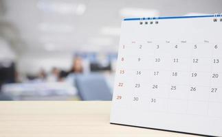 White paper desk calendar on wood table top with blurred office interior background photo