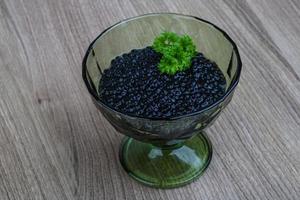 Black caviar in a bowl on wooden background photo