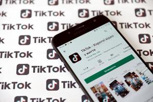 TERNOPIL, UKRAINE - MAY 2, 2022 Tik Tok smartphone app on screen and Many TikTok logo printed on paper. Tiktok or Douyin is a famous Chinese short-form video hosting service owned by ByteDance photo