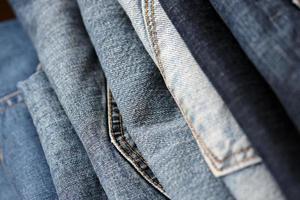 Many jeans in stack in wardrobe room. Row of pants denim jeans in closet. Concept of buy, sell, shopping and fashionable clothes photo