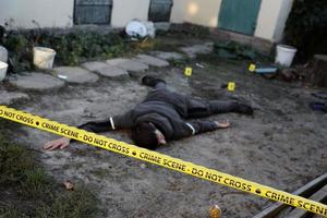 Victim of a violent crime in a backyard of residental house in evening. Dead man body under the yellow police line tape and evidence markers on crime scene photo