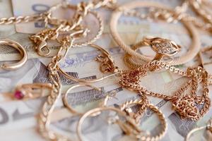 Many expensive golden jewerly rings, earrings and necklaces with big amount of Ukrainian money bills. Pawnshop or jewerly shop concept. Jewelry trading photo