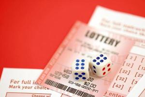 Red lottery ticket with dice lies on pink gambling sheets with numbers for marking to play lottery. Lottery playing concept or gambling addiction. Close up photo