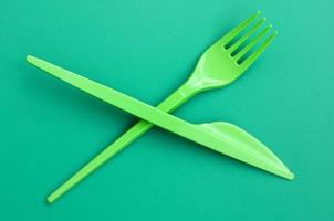 Disposable plastic cutlery green. Plastic fork and knife lie on a green background surface photo