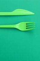 Disposable plastic cutlery green. Plastic fork and knife lie on a green background surface photo