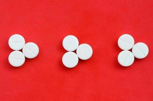 Several white tablets lie on a bright red background in the form of three triangular arrows. Background image on medicine and pharmaceutical topics photo