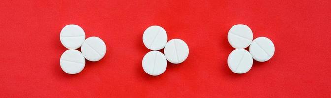 Several white tablets lie on a bright red background in the form of three triangular arrows. Background image on medicine and pharmaceutical topics photo