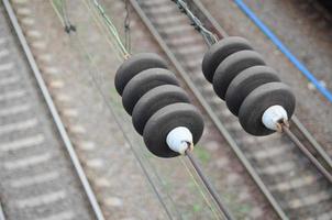 Electrical insulators on the contact wires on the background of a blurred railway track. Macro photo with selective focus