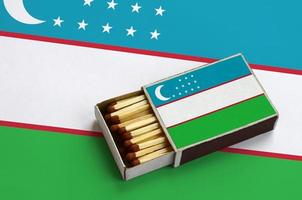 Uzbekistan flag  is shown in an open matchbox, which is filled with matches and lies on a large flag photo