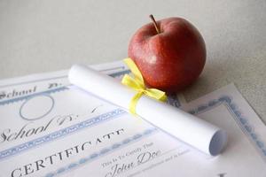 A honor roll recognition, certificate of achievement and high school diploma lies on table with small scroll and red apple. Education documents photo