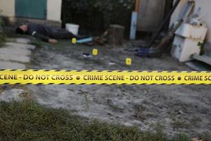 Victim of a violent crime in a backyard of residental house in evening. Dead man body under the yellow police line tape and evidence markers on crime scene photo