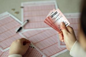 llenando un boleto de lotería. una mujer joven sostiene el billete de lotería con una fila completa de números en el fondo de las hojas en blanco de la lotería. foto