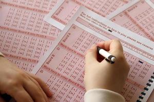 Filling out a lottery ticket. A young woman plays the lottery and dreams of winning the jackpot. Female hand marking number on red lottery ticket photo