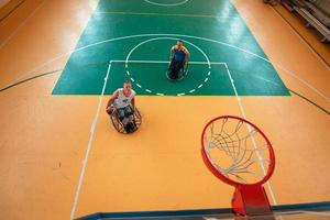 veteranos de guerra o de trabajo discapacitados equipos mixtos de baloncesto de raza y edad en sillas de ruedas jugando un partido de entrenamiento en un gimnasio deportivo. concepto de rehabilitación e inclusión de personas con discapacidad. foto