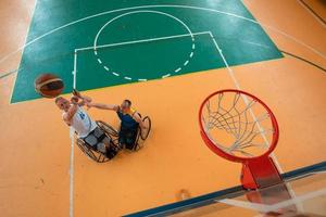 veteranos de guerra o de trabajo discapacitados equipos mixtos de baloncesto de raza y edad en sillas de ruedas jugando un partido de entrenamiento en un gimnasio deportivo. concepto de rehabilitación e inclusión de personas con discapacidad. foto