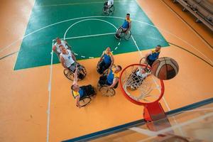 Disabled War or work veterans mixed race and age basketball teams in wheelchairs playing a training match in a sports gym hall. Handicapped people rehabilitation and inclusion concept.