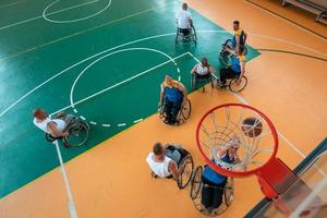 veteranos de guerra o de trabajo discapacitados equipos mixtos de baloncesto de raza y edad en sillas de ruedas jugando un partido de entrenamiento en un gimnasio deportivo. concepto de rehabilitación e inclusión de personas con discapacidad. foto