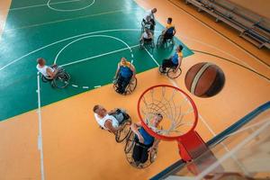 veteranos de guerra o de trabajo discapacitados equipos mixtos de baloncesto de raza y edad en sillas de ruedas jugando un partido de entrenamiento en un gimnasio deportivo. concepto de rehabilitación e inclusión de personas con discapacidad. foto