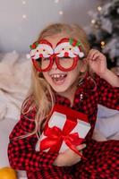 happy little blonde girl at home in pajamas for Christmas sorting presents and playing with Christmas toys photo