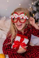 happy little blonde girl at home in pajamas for Christmas sorting presents and playing with Christmas toys photo