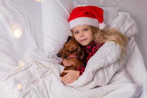 niña duerme en la cama con un perro salchicha para navidad foto