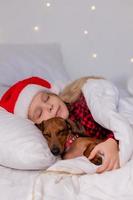 niña duerme en la cama con un perro salchicha para navidad foto