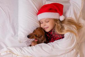 niña duerme en la cama con un perro salchicha para navidad foto