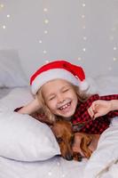 little girl sleeps in bed with a dachshund dog for Christmas photo