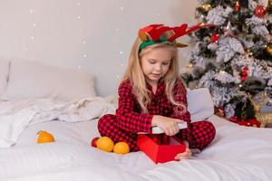 happy little blonde girl at home in pajamas for Christmas sorting presents and playing with Christmas toys photo