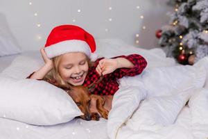 niña duerme en la cama con un perro salchicha para navidad foto