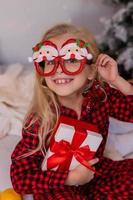 happy little blonde girl at home in pajamas for Christmas sorting presents and playing with Christmas toys photo