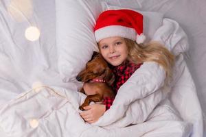 little girl sleeps in bed with a dachshund dog for Christmas photo