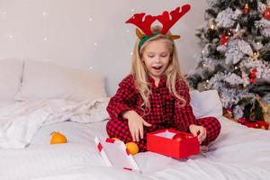 happy little blonde girl at home in pajamas for Christmas sorting presents and playing with Christmas toys photo
