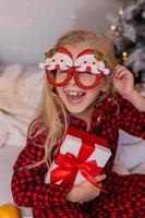 happy little blonde girl at home in pajamas for Christmas sorting presents and playing with Christmas toys photo