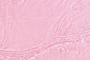 desenfoque borroso transparente color rosa claro agua tranquila textura superficial con salpicaduras, burbujas. fondo de ondulación de agua rosa brillante. superficie del agua en la piscina. agua de burbujas rosadas que brilla. foto