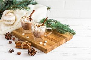 traditional New Year's drink with marshmallow on a wooden board against the background of a white brick wall, spruce branches and Christmas toys.