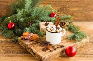 white enameled mug with hot chocolate or cocoa, pieces of chocolate and cinnamon sticks on a wooden board. the concept of a cozy Christmas.