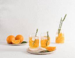 two glasses in the shape of a jar with orange vitamin water and ice cubes on a white ceramic tray. detox water. photo