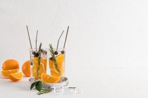 two modern cocktail glasses with a soft soft drink with orange slices and blueberries on a white table opposite the brick wall. photo