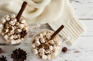 two large mugs with chocolate drink and marshmallow on the wooden country table and a knitted sweater. the concept of a cozy Christmas. photo