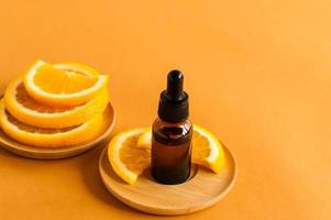 serum with vitamin C, a bottle of orange essential oil and slices of fresh fruit on an orange background. photo