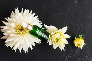 anti-aging serum in a cosmetic bottle with a pipette on a black background and a beautiful white dahlia. top view. photo