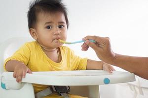 una linda chica blanca sentada en una silla desayunando en el hogar interior alimentando deliciosas comidas que son altamente nutritivas el bebé tiene una cara alegre, divertida, sonriente y feliz en un estilo de vida familiar saludable. foto