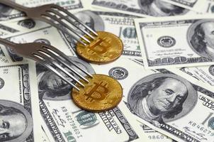 Bitcoin getting New Hard Fork Change, Physical Golden Crytocurrency Coin under the fork on the dollars background. Blockchain Transaction System Crisis Concept photo
