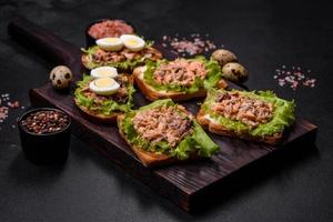 Delicious fresh sandwiches with toast, canned salmon, salad and quail eggs photo