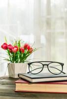 Reading glasses put on hardcover book beside the window photo