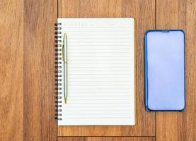 Top view image of open notebook with blank pages and cellphone on wooden table photo