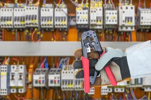 Hand in glove holding  wire stripper with control panel cabinet photo