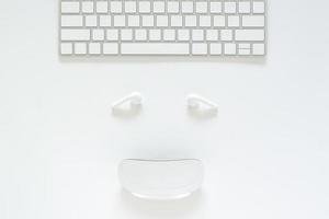 disposición plana de teclado, auricular y mouse configurados como cara sonriente sobre fondo blanco para el concepto de venta en línea del lunes cibernético. foto